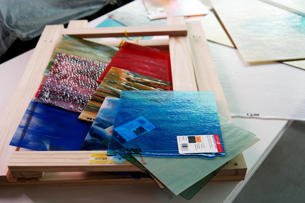 Colourful glass sheets and craft materials arranged on workshop table showing artistic production materials
