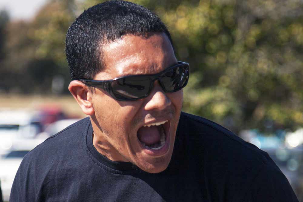 Male spectator in sunglasses cheering enthusiastically at SAESI firefighter competition outdoor event