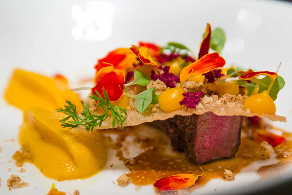 Seared beef with edible flowers, butternut purée and colourful garnish, professional restaurant photography